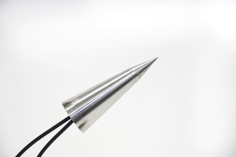 May include: A silver metal cone with a pointed tip and two black wires attached to the base.