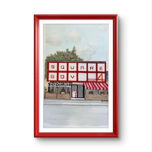 May include: Watercolor painting of a building with the words "SQUARE BOY" in red and white block letters. The building has a red and white striped awning and a "4" sign. The artwork is framed in a red frame.