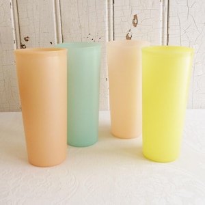 May include: Four tall, pastel-colored drinking glasses. The glasses are in shades of peach, mint green, pale pink, and yellow. They are cylindrical in shape and appear to be made of a translucent material.