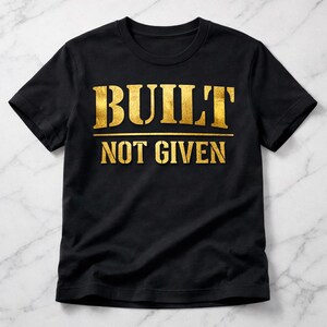 May include: Black t-shirt with gold text that reads "BUILT" above "NOT GIVEN". The text is in a bold, sans-serif font. The shirt is made of a soft material and has short sleeves.