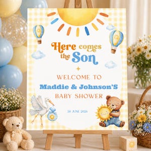 May include: A baby shower sign on a wooden easel. The sign reads "Here comes the Son" and welcomes guests to Maddie & Johnson's baby shower on June 30, 2026. The sign features illustrations of a sun, hot air balloons, a stork, and a teddy bear.