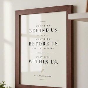 May include: A framed print with a dark brown wooden frame. The print features the quote "WHAT LIES BEHIND US AND WHAT LIES BEFORE US ARE TINY MATTERS COMPARED TO WHAT LIES WITHIN US." by Ralph Waldo Emerson.