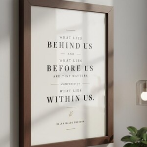 May include: A framed print with a dark brown wooden frame. The print features the quote "WHAT LIES BEHIND US AND WHAT LIES BEFORE US ARE TINY MATTERS COMPARED TO WHAT LIES WITHIN US." by Ralph Waldo Emerson, in a minimalist design.