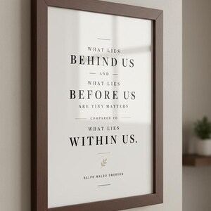 May include: A framed print with a dark brown wooden frame. The print features the quote "WHAT LIES BEHIND US AND WHAT LIES BEFORE US ARE TINY MATTERS COMPARED TO WHAT LIES WITHIN US." by Ralph Waldo Emerson, in black text.