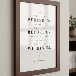 May include: A framed print with a dark brown wooden frame. The print features the quote "What lies behind us and what lies before us are tiny matters compared to what lies within us." by Ralph Waldo Emerson, in black text on a white background.