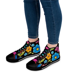 May include: Black high-top trainers with a colourful floral design. The trainers have a black sole and laces, with bright flowers in blue, yellow, pink, and orange on a black backdrop. The shoes are worn with blue jeans.
