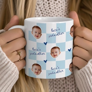 May include: A white ceramic mug featuring a light blue and white checkered pattern. The mug is decorated with repeating photographs of a baby's face, small dark blue heart icons, and the repeating blue cursive text "luca's godmother".