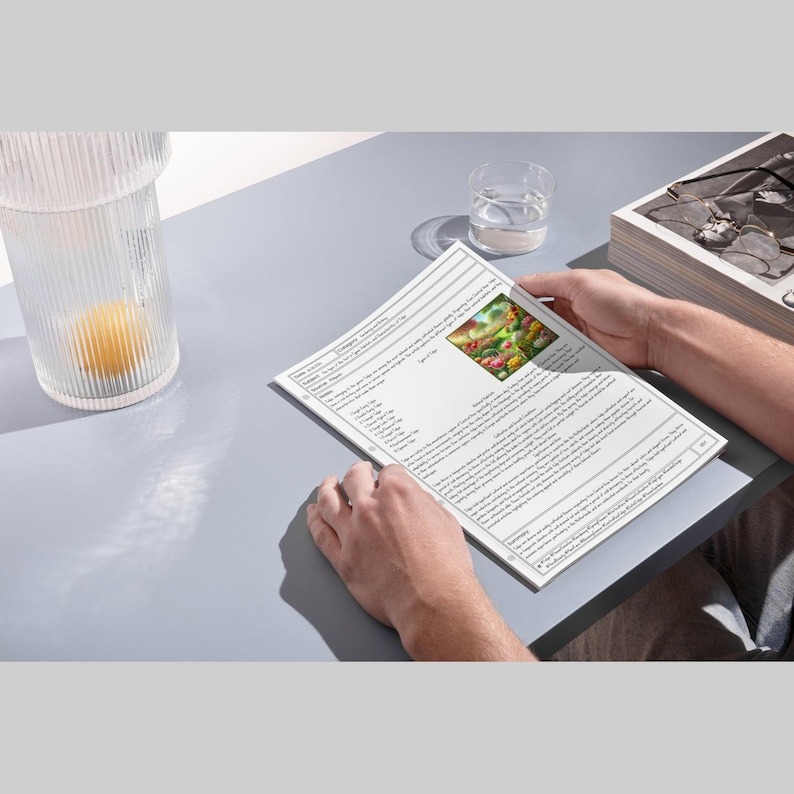 May include: A person holding a printed document with text and an image of colorful flowers. The document is on a grey surface, with a glass of water and a decorative glass container with a yellow object inside.