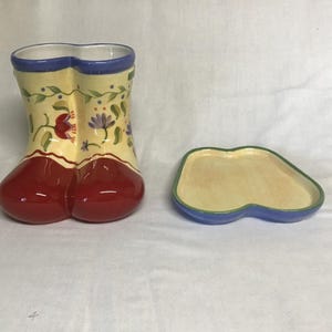 May include: A ceramic boot-shaped vase and matching tray. The vase is red at the base, with a yellow body decorated with floral patterns and a blue rim. The tray has a similar design with a blue rim and green edge.