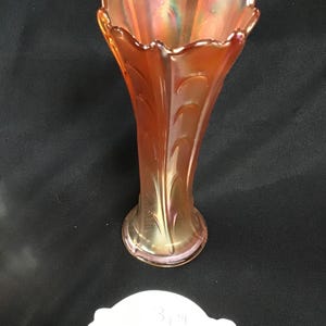 May include: An iridescent orange glass vase with a ruffled rim and a flared body. The vase has a decorative leaf pattern and a round base. The vase is approximately 3 inches tall.