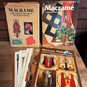 May include: A collection of vintage macramé books. Titles include "Macramé: Creative Design in Knotting" and "Macramé: Techniques and Projects." The books feature images of macramé projects, including wall hangings and plant holders. The books are in various conditions.