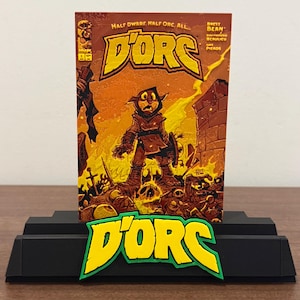 May include: A comic book titled D'ORC with a yellow logo and orange cover art featuring a hooded character standing amidst debris and skulls, displayed on a black stand with a matching yellow and green D'ORC logo attached to the front base.