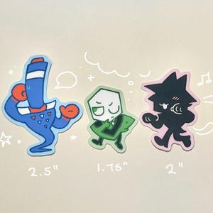 Puede incluir: Tres pegatinas de dibujos animados sobre un fondo claro. Las pegatinas son de diferentes personajes, incluyendo una figura azul con guantes rojos, una figura verde y una figura negra con un contorno rosa. Medidas: 6,35 cm, 4,45 cm y 5,08 cm.