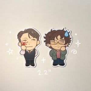 Może przedstawiać: Dwie naklejki z kreskówek, każda o wysokości 5,6 cm. Jedna przedstawia mężczyznę w garniturze z zakrwawioną twarzą, druga mężczyznę w okularach i zielonej kurtce. Naklejki są na jasnobeżowym tle.