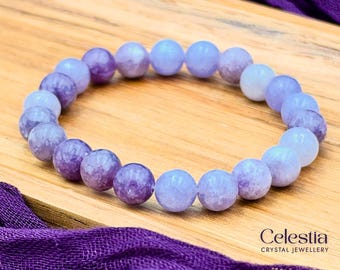 Puede incluir: Una pulsera de cuentas compuesta por piedras pulidas, redondas y lisas en tonos variados de morado claro, lavanda y violeta suave. Las cuentas están ensartadas en un bucle circular. El texto Celestia Crystal Jewellery es visible.