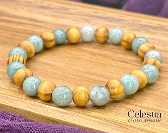 May include: A stretch bracelet featuring alternating round beads made of light brown wood and smooth, pale green stone. The beads are arranged in a repeating pattern, with a single white bead at the top. The text Celestia Crystal Jewellery is visible.