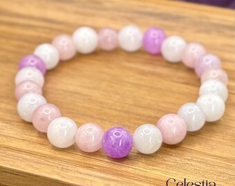Puede incluir: Un brazalete de cuentas con cuentas de piedras preciosas blancas, rosa claro y moradas. El brazalete se muestra sobre una superficie de madera. La marca "Celestia Crystal Jewellery" es visible en la esquina inferior derecha.