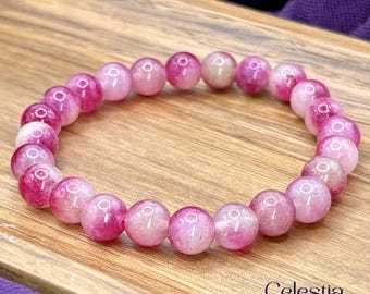 Puede incluir: Una pulsera elástica compuesta por cuentas redondas y pulidas en varios tonos de rosa y magenta. Las cuentas presentan un acabado liso y brillante con sutiles variaciones internas. El texto Celestia Crystal Jewellery es visible en la esquina.