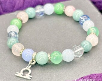 May include: A beaded bracelet featuring a variety of colorful gemstones, including green, blue, pink, and clear beads. The bracelet has a silver charm with the Libra zodiac symbol. The Celestia Crystal Jewellery logo is visible in the bottom right corner.