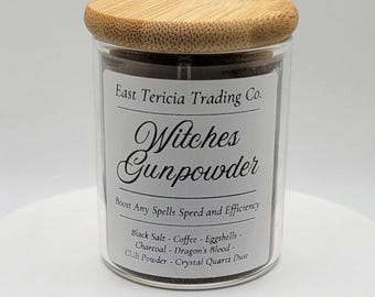 May include: A clear glass jar with a light brown bamboo lid containing dark powder. The white label reads East Tericia Trading Co. Witches Gunpowder, Boost Any Spells Speed and Efficiency, Black Salt, Coffee, Eggshells, Charcoal, Dragon's Blood, Chili Powder, Crystal Quartz Dust.