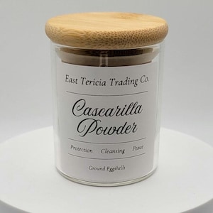 May include: A clear glass jar with a bamboo lid, labeled "East Tericia Trading Co." and "Cassearilla Powder." The label also includes the words "Protection, Cleansing, Peace" and "Ground Eggshells."