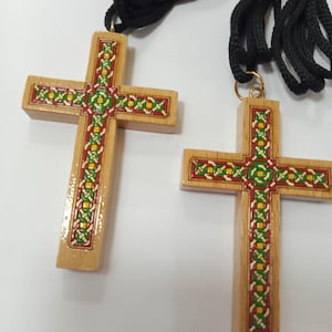 May include: Two wooden cross pendants with a decorative red, green, and yellow border design. Each cross is attached to a black cord. The crosses are made of light-colored wood.