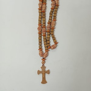 May include: A wooden rosary with a cross pendant. The rosary features alternating square and round beads in shades of brown and orange. The cross pendant is a detailed carving of a crucifix.