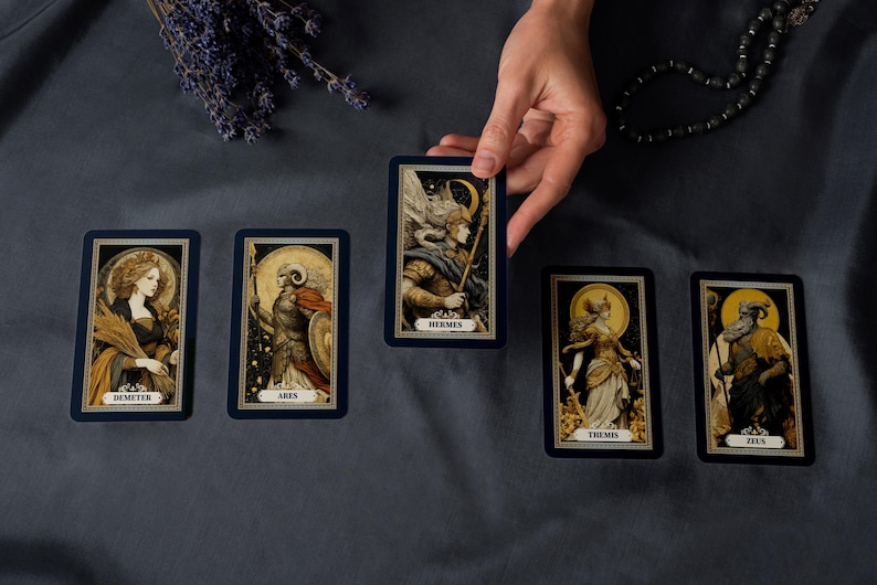 May include: A hand holding a tarot card with the name "Hermes" on it, surrounded by other tarot cards. The cards feature illustrations of figures with names like "Demeter", "Ares", "Themis", and "Zeus". The cards have a dark blue border.
