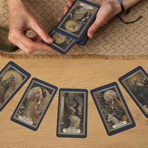May include: A collection of tarot cards with dark blue borders and detailed illustrations. The cards feature images of mythological figures and celestial elements. The cards are arranged on a wooden surface with a decorative cloth and a peacock feather.