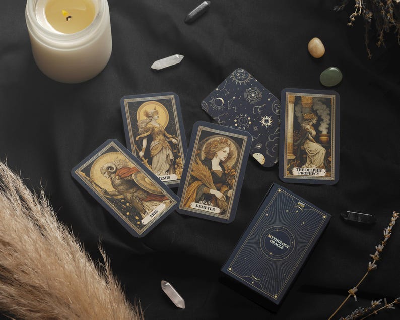 May include: A collection of mythology oracle cards with illustrations of figures and celestial designs. The cards are arranged on a black surface with a candle, crystals, and dried plants. The card box reads "Mythology Oracle".