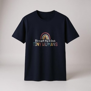 May include: Navy blue t-shirt with a rainbow graphic and the text "It's a good day to teach TINY HUMANS" in colorful letters. The shirt has short sleeves and a crew neck.