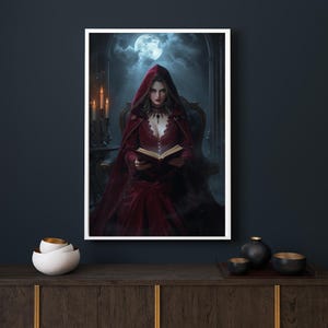 Könnte beinhalten: Ein gerahmter Druck zeigt eine Frau in einem roten Kapuzenmantel, die ein Buch liest. Die Szene wird von Kerzenlicht und einem Vollmond beleuchtet. Die Frau trägt eine dunkle Halskette und ein rotes Kleid. Der Hintergrund ist ein dunkles, gotisches Interieur.