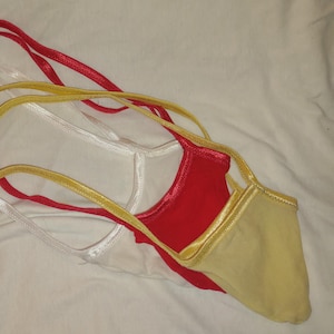 May include: A set of three thong-style undergarments featuring thin elastic straps. The garments are coloured in solid white, bright red, and pale yellow. Each piece is constructed with a small fabric pouch and slender waist and side straps.