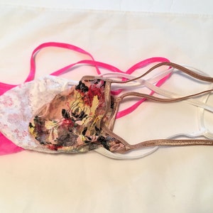 May include: Three pairs of lingerie with different patterns and colors. One pair is pink with white lace, another is floral with brown and white, and the last is white with a brown trim.