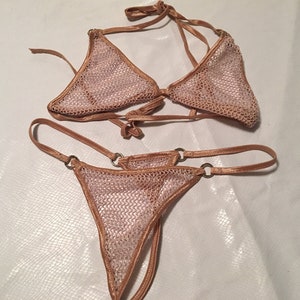 May include: A nude-colored mesh bikini set with adjustable straps and metal rings. The top is a triangle style and the bottom is a cheeky cut.