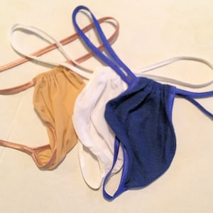 May include: Three pairs of underwear in different colors: tan, white, and blue. The underwear is made of a soft, stretchy fabric and has a simple design.