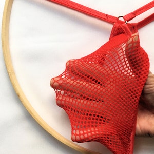 May include: Red mesh underwear with a thin red strap and a metal ring.