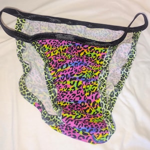 May include: A pair of underwear with a vibrant leopard print in neon colors, including pink, yellow, green, and blue. The edges are trimmed with black elastic.
