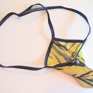 May include: Yellow and black thong underwear with a tiger stripe pattern. The underwear has a black elastic waistband and straps. The fabric is a sheer, lightweight material.