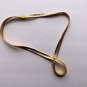 May include: A gold-colored chain necklace with a simple design. The chain is made of a thin, flexible material and has a smooth finish.