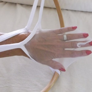 May include: A white fabric hoop with a white fabric strap attached to it. The strap is looped around a hand with red nail polish.