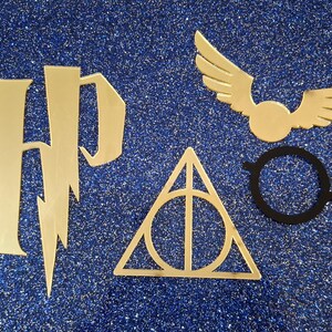 May include: Gold-coloured Harry Potter logo, Deathly Hallows symbol, and winged golden snitch, alongside black round glasses, set against a sparkly blue background. The image features iconic symbols from the popular fantasy series.