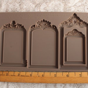 May include: A brown silicone mold with three ornate frame designs. The mold is approximately 8 inches long and features a raised inscription that reads "Copyright 2013 All rights reserved.  Designed by LySandra.  For personal use only.  ITEM NO. 665126 LYSANDRA. www.prettylittleframes.com".