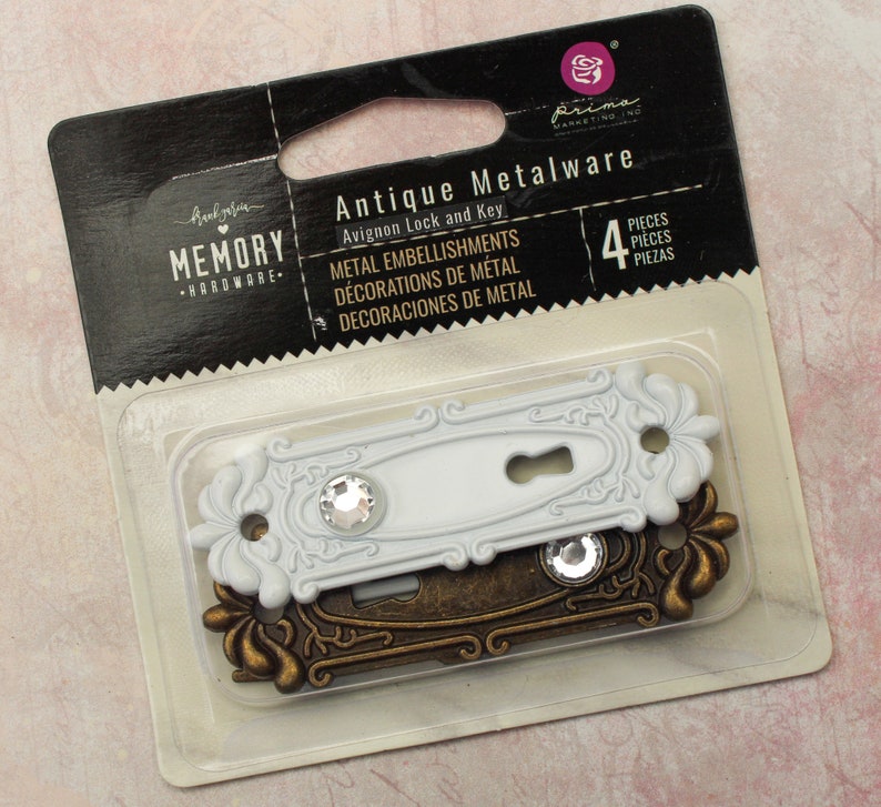 May include: A package of four antique metalware embellishments. The set includes two Avignon lock and key designs. One is white with a crystal accent, and the other is bronze-colored. The package is labeled "Memory Hardware."