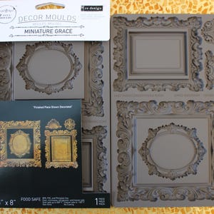 Könnte beinhalten: Graue Silikonformen mit verzierten Rahmenmotiven. Die Verpackung enthält eine Karte mit Bildern von fertigen, dekorierten Rahmen. Die Formen sind mit "MINIATURE GRACE" gekennzeichnet und messen 12,7 cm x 20,3 cm.