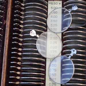 May include: A close-up of an eye chart with a series of lenses in a wooden frame. The lenses are arranged in rows and columns, and the chart includes a scale of numbers from 0.25 to 5.50.