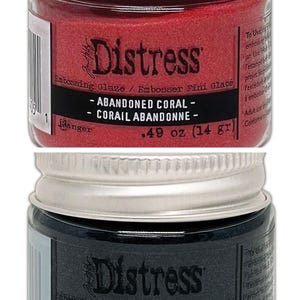 Op de afbeelding: Twee kleine potjes Distress Embossing Glaze. De bovenste pot is rood en heeft het label "Abandoned Coral - Corail Abandonn&eacute; - 0,49 oz (14 g)". De onderste pot is donkerblauw en heeft het label "Chipped Sapphire - &Eacute;clat de Saphir - 0,49 oz (14 g)".