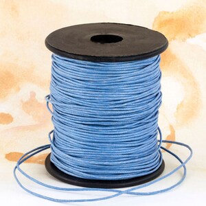 May include: A spool of light blue waxed cotton cord. The cord is tightly wound around a black plastic spool. The background is a watercolor wash of beige and brown.