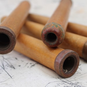 May include: A collection of vintage wooden spools with dark brown metal ends. The spools are cylindrical, with a light brown color and visible wood grain. Some spools have a reddish-brown hue on the ends, and some have green paint.