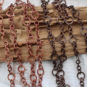 Op de afbeelding: Twee strengen koperen ketting met getextureerde, ronde schakels. De ketting wordt getoond op een stuk drijfhout.